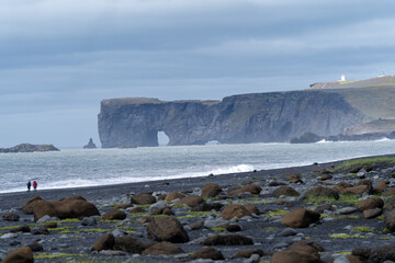 Fototapeta na wymiar Black sand beach looking toward sea stacks and arches, in Vik, Iceland, Dyrholaey. Unidentifiable people for scale