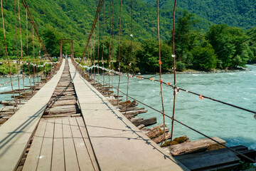old wooden suspension bridge hanging over mountaing fast river 