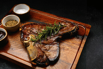 succulent grilled T-bone steak with rosemary and spices served on dark wooden board. close up