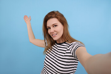 Fototapeta premium Beautiful woman taking selfie on light blue background