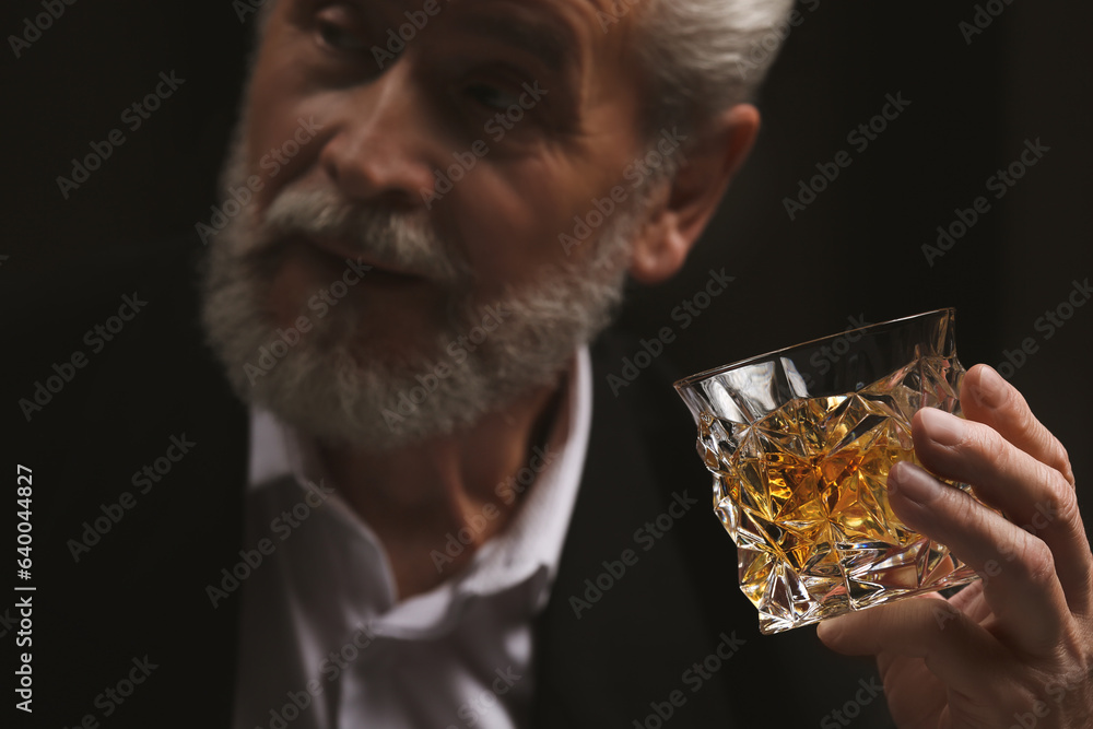 Sticker Man in suit holding glass of whiskey with ice cubes on black background, selective focus