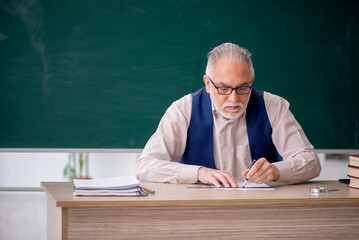 Old male teacher in front of green board