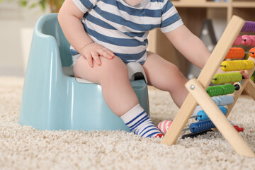 Little child sitting on plastic baby potty indoors, closeup