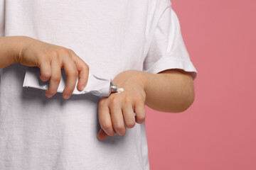 Child applying ointment onto hand against pink background, closeup. Space for text