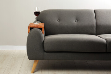Glass of red wine on sofa with wooden armrest table in room. Interior element