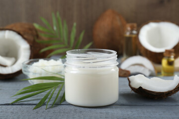 Jar of organic coconut cooking oil, leaves and fresh fruits on grey wooden table, closeup