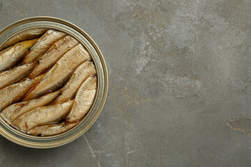 Sprats in tin can on grey textured table, top view. Space for text