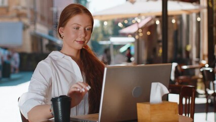 Pretty redhead child girl start begin work online distant job open laptop in city street cafe restaurant browsing website chatting outdoors during break. Young smiling woman tourist looking at camera
