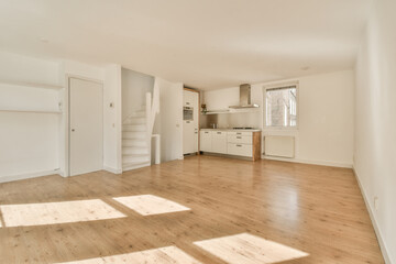 an empty living room with wood flooring and white cupboards on either side of the door to the kitchen