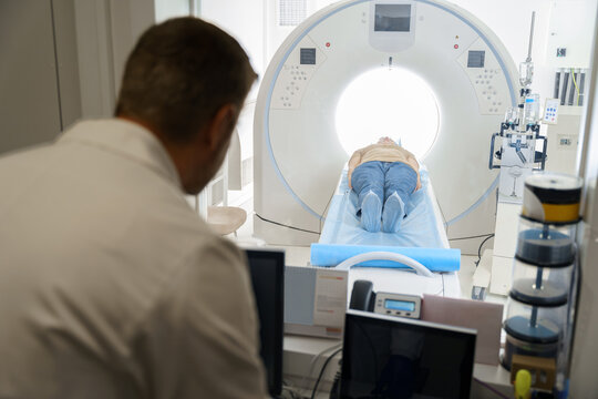 Radiologist controls MRI or CT Scan with patient undergoing procedure. High Tech medical equipment