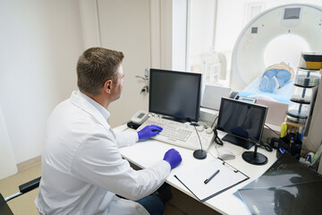 Fototapeta na wymiar Radiologist controls MRI or CT Scan with patient undergoing procedure. High Tech medical equipment