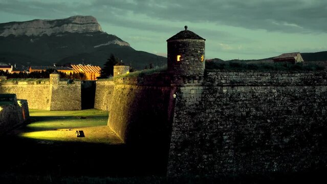 View of stone walls of medieval fortified star-shaped Castle of San Pedro de Jaca with corner turret on background of Oroel rock covered with green forest in summer twilight, province of Huesca, Spain