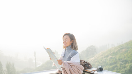 Girl tourist in mountain read the map and looking mountain view at countryside homestay in the morning sunrise with copy space. journey, trip and relaxing concept. coats blankets in winter.