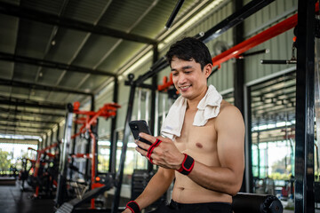 young male playing phone and listening to music after exercise with various exercise equipment in fitness.