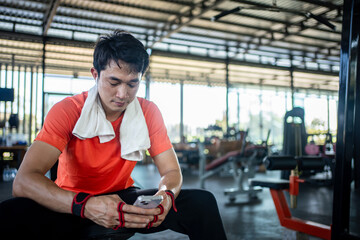young male playing phone and listening to music after exercise with various exercise equipment in fitness.