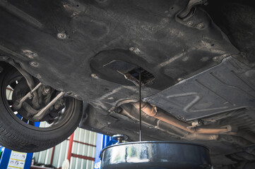 Auto mechanic draining an old and dirty engine oil flow out of the engine oil pan.