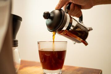 Pouring hot coffee from a french press jug into a drinking glass