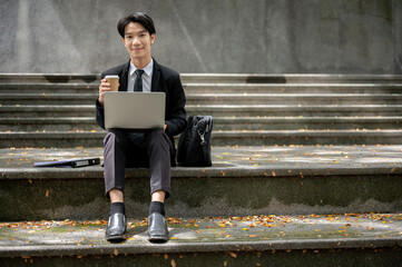 A busy Asian businessman sitting on stairs in front of the building, working remotely in the city.