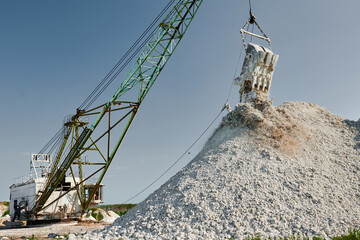 Walking excavator pours chalk from bucket against blue sky