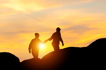 Fototapeta na wymiar Silhouette of a couple holding hands and walking together with blurred sunset background, Teamwork couple climbing helping hand