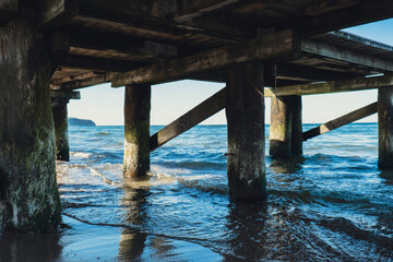 Storm sea waves under wooden pier in dramatic background wallpaper design. Seascape with running splashing sea waves. Sandy beach vacation getaway in Gdansk Poland. Copy space for your text 