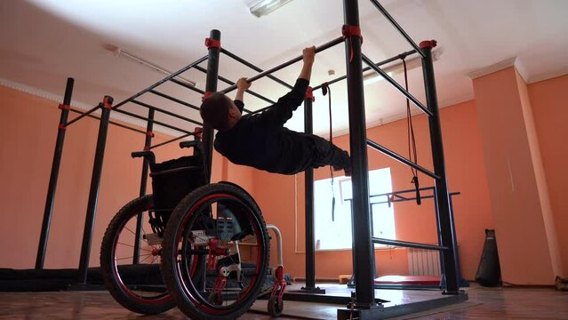 A young man in a wheelchair on a gymnastic pull-up bar in the gym performing exercises