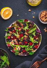 Vegan salad with beet, dried plums, arugula, swiss chard and walnuts, black stone table background. Fresh useful vegetarian dish for clean eating