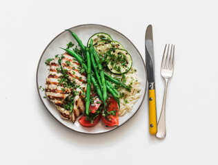Delicious balanced lunch - grilled chicken fillet, orzo, string beans, zucchini and tomatoes on a light background, top view