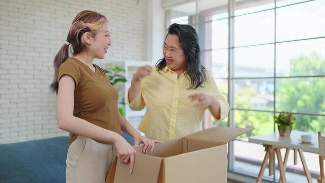 Young Asian woman with mature mother enjoy unpacking parcel together. Happy elderly mom and daughter excited unpacking cardboard box receiving ordered from internet store. Online Shopping