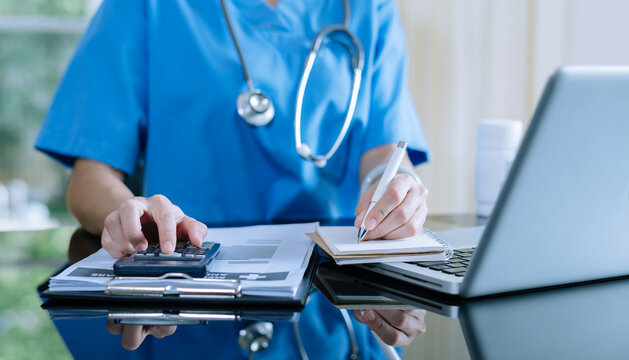 Healthcare costs and fees concept.Hand of smart doctor used a calculator and smartphone, tablet for medical costs at hospital in morning light - Powered by Adobe