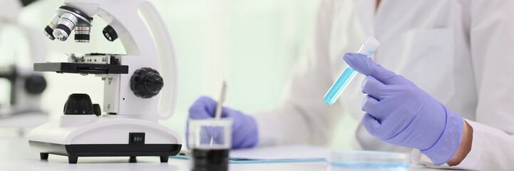 A woman in front microscope and blue reagent in test tube