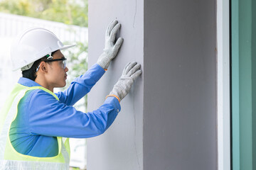 An engineer wearing a blue shirt and a white hat is inspecting the building's crack condition.