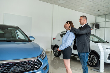 man and woman couple holding key to their car looking at camera and smiling in car showroom.