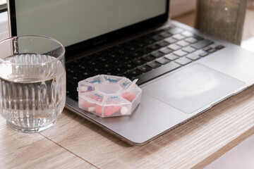 Woman taking Daily vitamins white working on laptop Organizer weekly shots Closeup of medical pill box with doses of tablets for daily take medicine with white pink drugs and capsules. Workplace