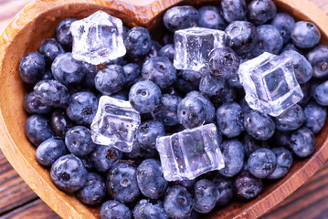 Freshly picked blueberries with ice cubes in heart shaped wooden plate, top view