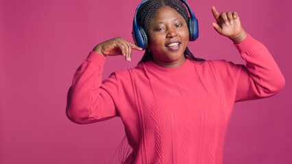 Joyful black woman wearing modern earphones moving around and having a good time. Lady with african american ethnicity confidently dancing to good music from stereo headphones.