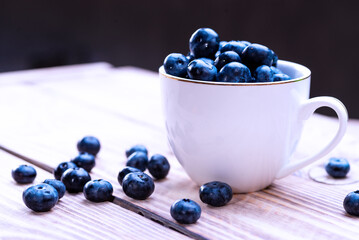 Freshly picked organic blueberries in a white cup on a light wooden table