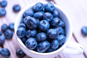 Freshly picked organic blueberries in a white cup on a light wooden table