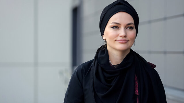 Muslim woman wearing black hijab and dark clothes walking past grey city building, copyspace