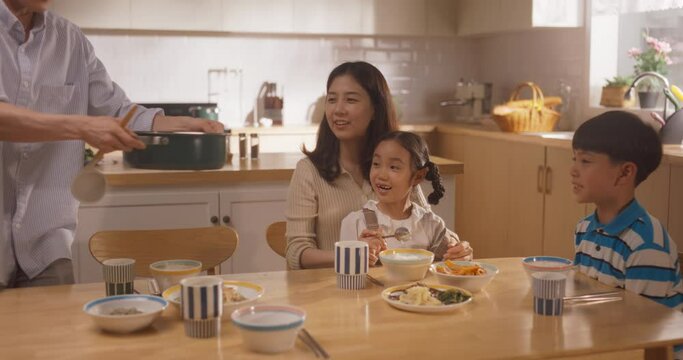 Happy Korean Family of Four Enjoying a Delicious Meal Together in Their Kitchen at Home. They are Sharing a Traditional Meal Made with Love and Care. Children Excited for Food