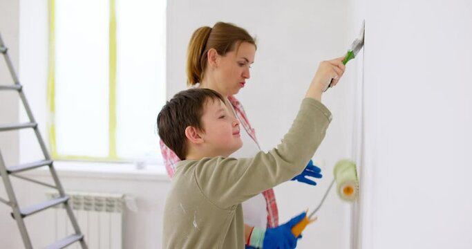 Happy family mother and son paint the wall with paint using roller and brush