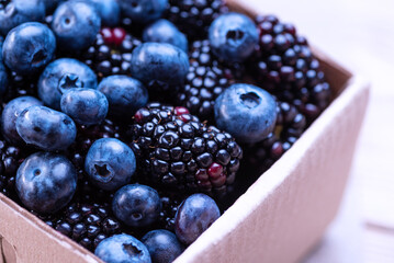 Blueberries and blackberries in a cardboard box on a wooden table. Mixture of blue berries close-up
