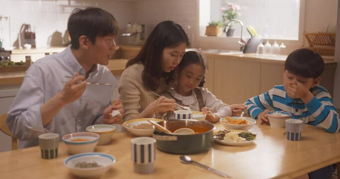 Happy Korean Family of Four Enjoying a Delicious Meal Together in Their Kitchen at Home. Parents and Their Cute Children Gathered For Lunch, Eating and Talking While Sitting at the Table