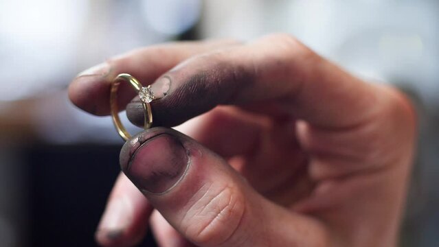 Closeup of a diamond wedding ring and dirty jeweller hands holding it