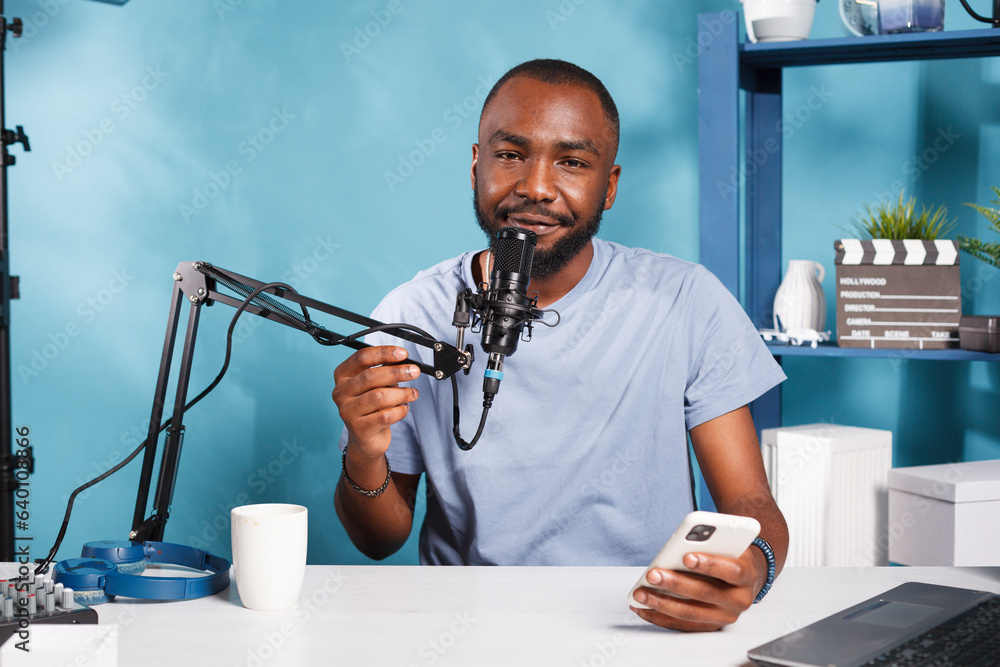 Poster cheerful vlogger speaking in microphone while reading from smartphone and streaming online portrait.
