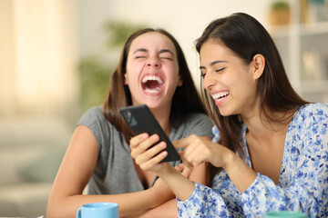 Two happy friends laughing hilarious using phone at home
