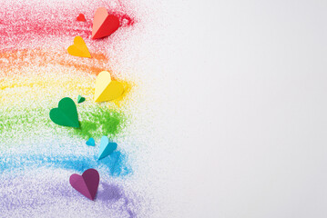 Top view of sand flag celebrates LGBT history month. Colorful sand forms a rainbow flag and small hearts on white, with an open circle for empowering and inclusive messages