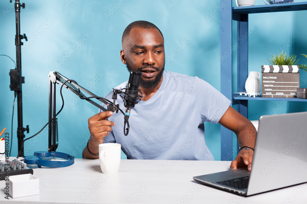 Poster internet influencer speaking in microphone and using laptop while recording video for blog in home s