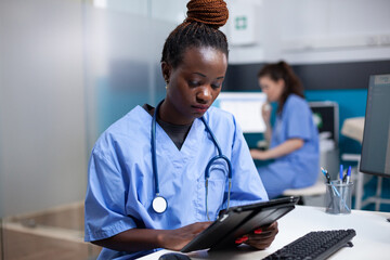 African american nurse working on digital touchscreen tablet in professional healthcare hospital...