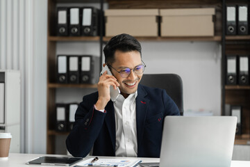 Smiling Asian young freelancer working from home remotely.He is talking on the phone.